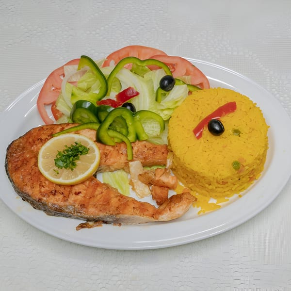 Grilled salmon steak with a lemon slice, yellow rice, and a side salad on a white plate.