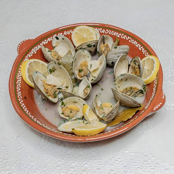 Steamed clams with lemon wedges and herbs in a decorative orange and green ceramic dish.