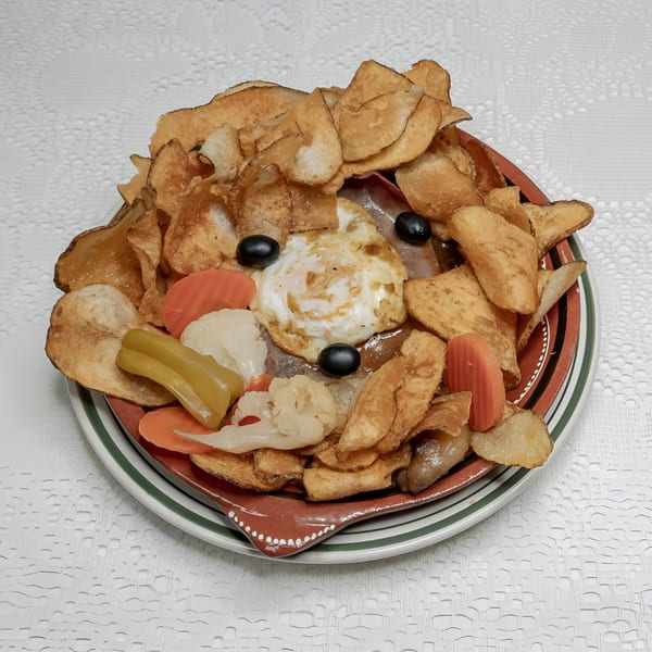 A large platter of Fords BBQ with crispy chips, fried egg, olives, and pickled vegetables.