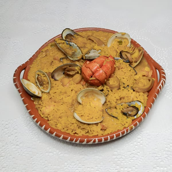 Seafood paella with lobster, mussels, and clams in a rustic orange dish on a white tablecloth.
